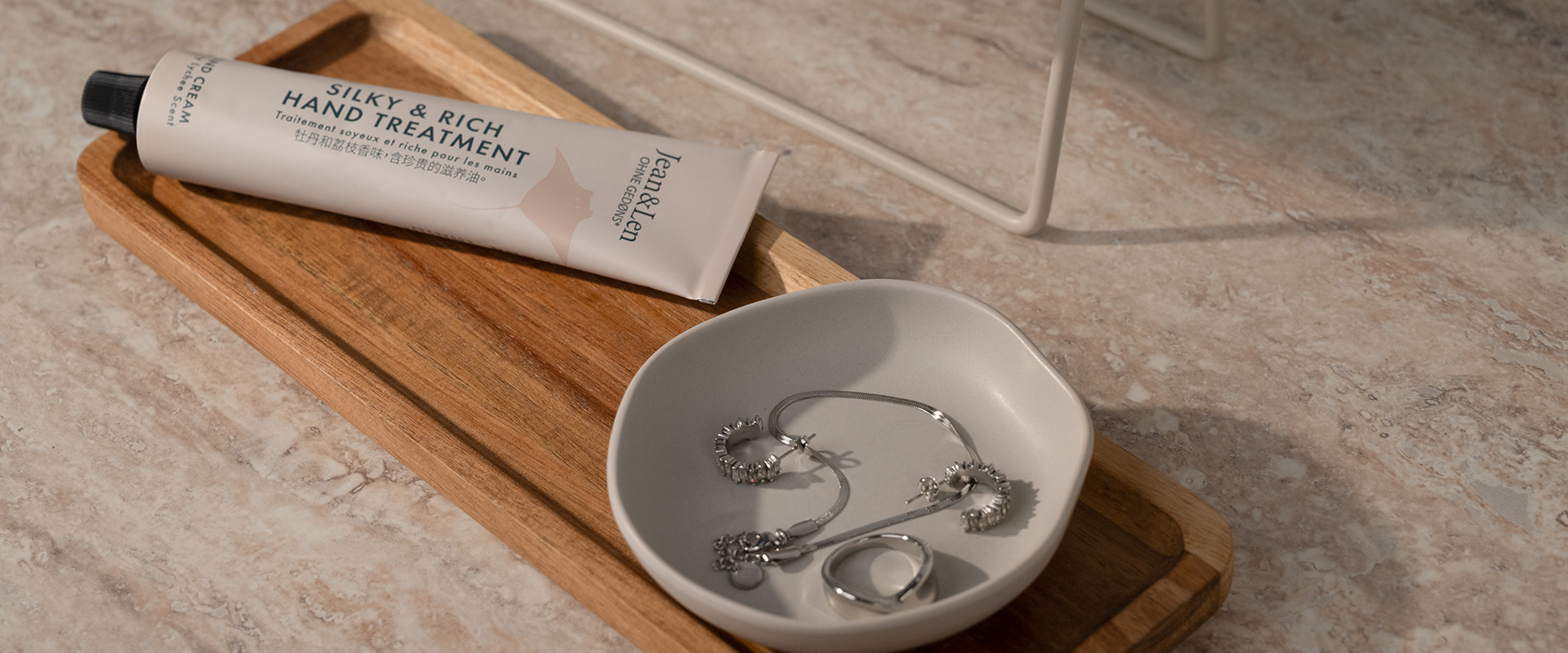 Schmuckschale mit Silberring, Kette und Ohrringen auf einem Holztablett; daneben eine Handcreme und ein Spiegel.