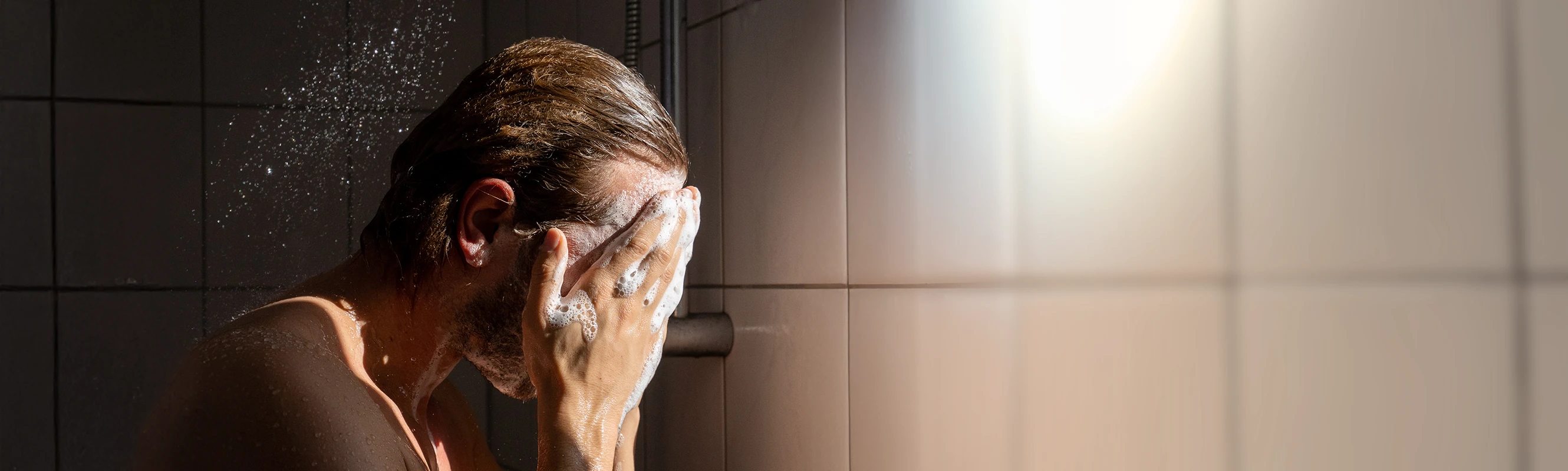 Mann schäumt sich unter der Dusche ein.