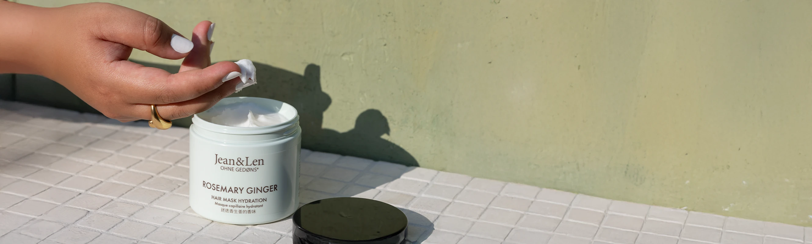 Eine feminine Hand entnimmt Haarkur aus dem Tiegel der Rosemary/Ginger Haarkur.